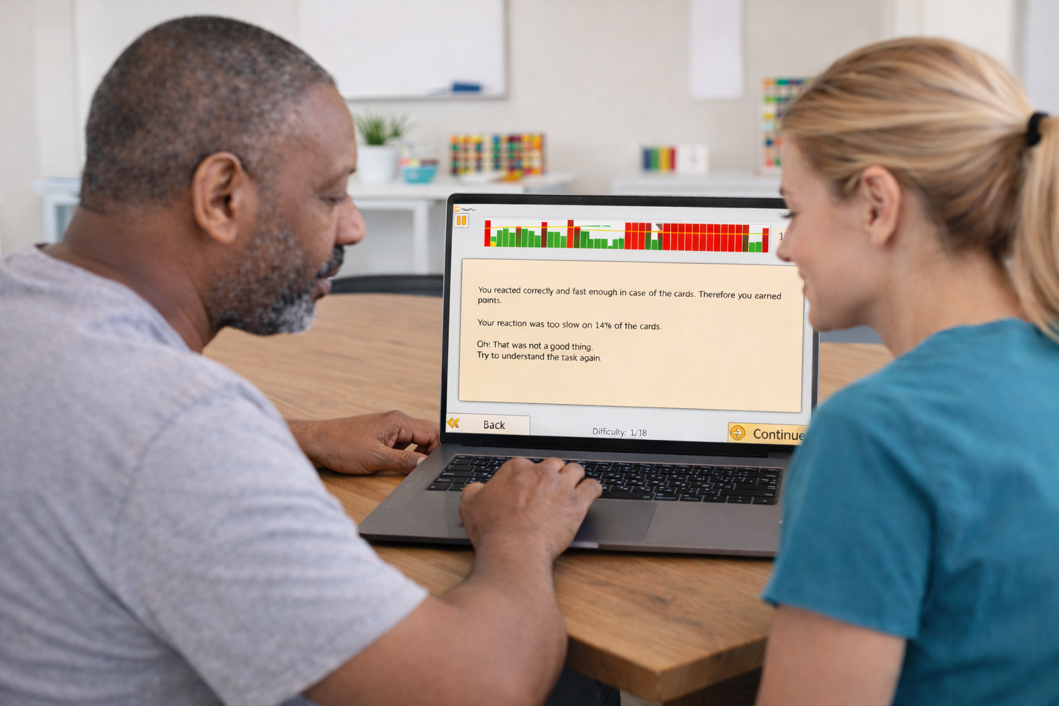 Therapist and patient reviewing HeadApp Hit It results together on a laptop, showing reaction-time feedback at difficulty 1 of 18